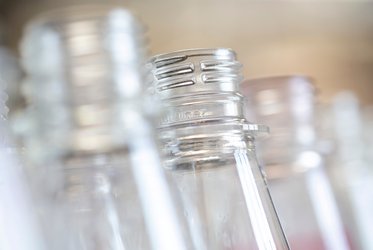 Das Bild zeigt eine Nahaufnahme mehrerer PET-Flaschenhälse, die unscharf im Hintergrund angeordnet sind, mit Fokus auf die Details des Gewindes einer Flasche.