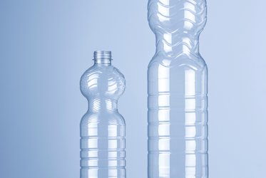 Das Bild zeigt eine kleine und eine größere transparente Kunststoffflasche auf einem hellblauem Hintergrund.