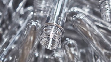 Das Bild zeigt eine Nahaufnahme mehrerer transparenter PET-Rohlinge, die für die Produktion von Flaschen verwendet werden und auf Recyclingmaterial hinweisen.