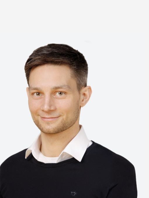 Das Bild zeigt den KHS-Kontakt Thyssen, ein junger Mann mit kurzem, dunkelbraunem Haar, der freundlich in die Kamera lächelt, gekleidet in einem schwarzen Pullover über einem weißen Hemd.