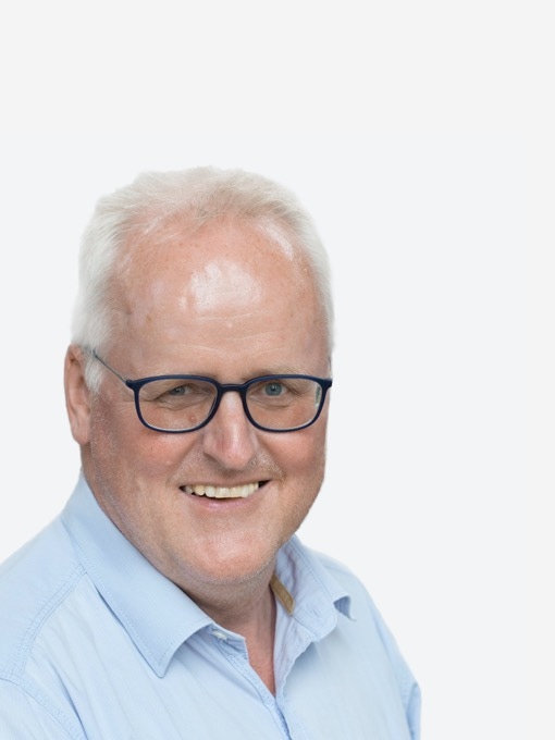 Der KHS-Kontakt Wickeren, ein Mann mit kurzen weißen Haaren, Brille und einem blauen Hemd lächelt freundlich in die Kamera vor einem weißen Hintergrund.